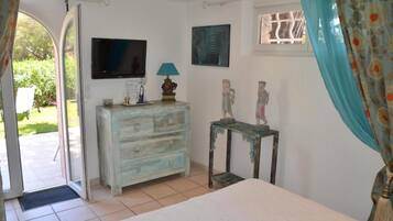 Un dormitorio con cama, cómoda, televisor y ventana con cortinas.
