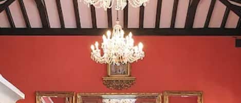 A bar area with wicker chairs, a chandelier, and a mirror reflecting the bar.