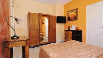 Une chambre d’hôtel avec un lit, une armoire en bois, un bureau avec une lampe, un téléviseur fixé au mur et un tableau.