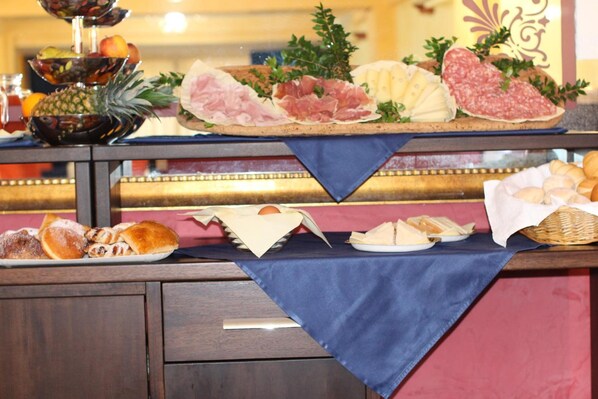 A buffet table with various food items including meats, cheeses, fruits, and pastries.