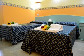 Habitación de hotel con dos camas, cada una con cubrecama de diseño azul y dorado, una mesita de noche con teléfono y un pequeño cubo de basura.