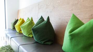 A row of green and yellow pillows on a leather sofa against a wooden wall.