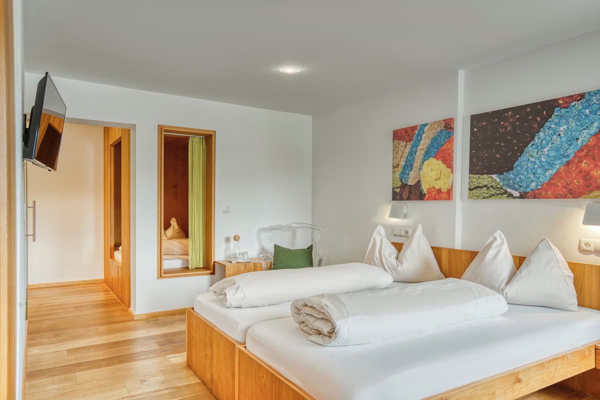 A modern hotel room with a wooden bed, a TV mounted on the wall, and a painting above the bed.