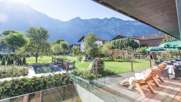 Un balcón con vistas a una cadena montañosa, un parque infantil y mobiliario exterior.