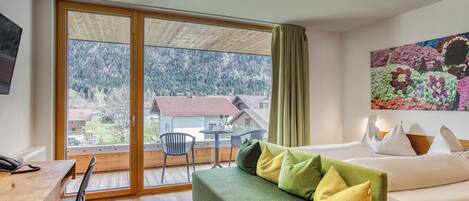 Una habitación con una cama, un escritorio y una silla. Hay una ventana que ofrece vistas a casas y árboles.