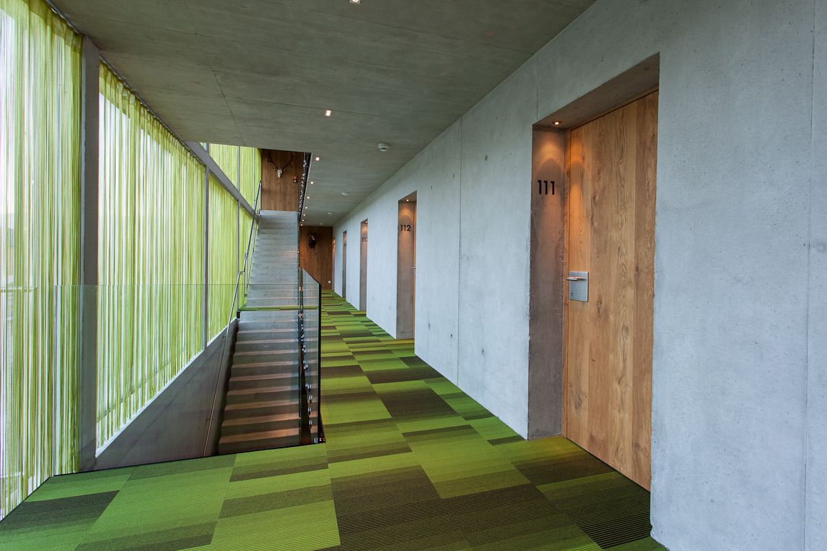 Un pasillo moderno con alfombra de estampado verde, una escalera y puertas de madera numeradas 111 y 112.