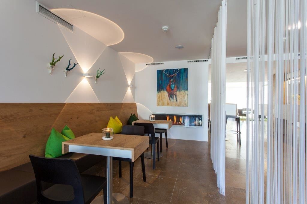 Un espace repas moderne avec un banc en bois, des chaises noires et une table agrémentée d’une bougie. Un tableau orne le mur et un foyer est visible à l’arrière-plan.