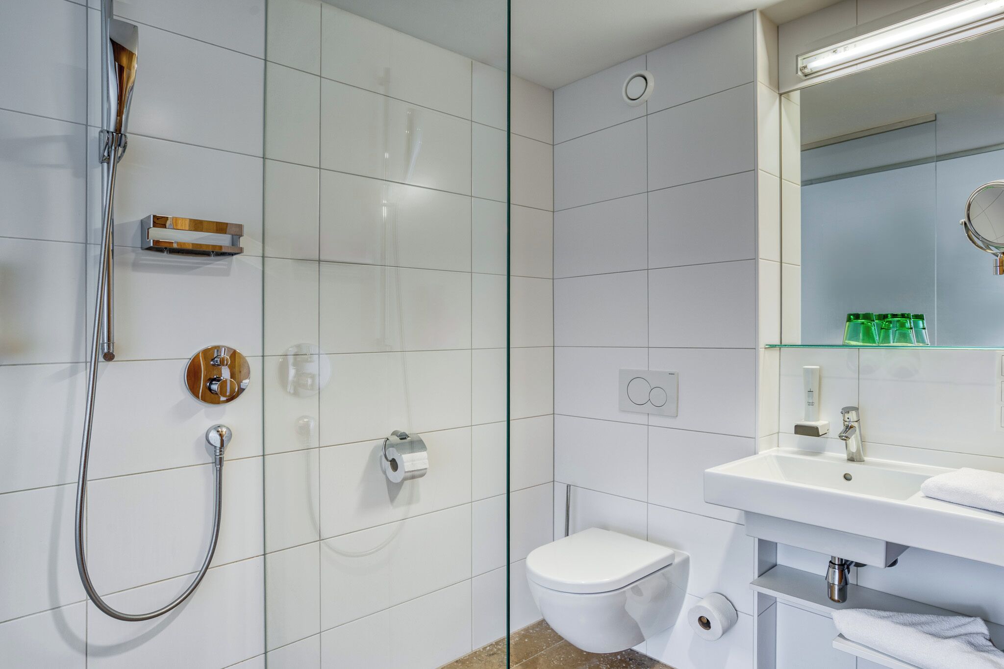 A modern bathroom with a glass-enclosed shower, a white toilet, and a sink with a mirror above it.