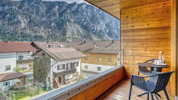 Een balkon met houten vloer en leuning, met uitzicht op een bergachtig landschap met verschillende gebouwen.