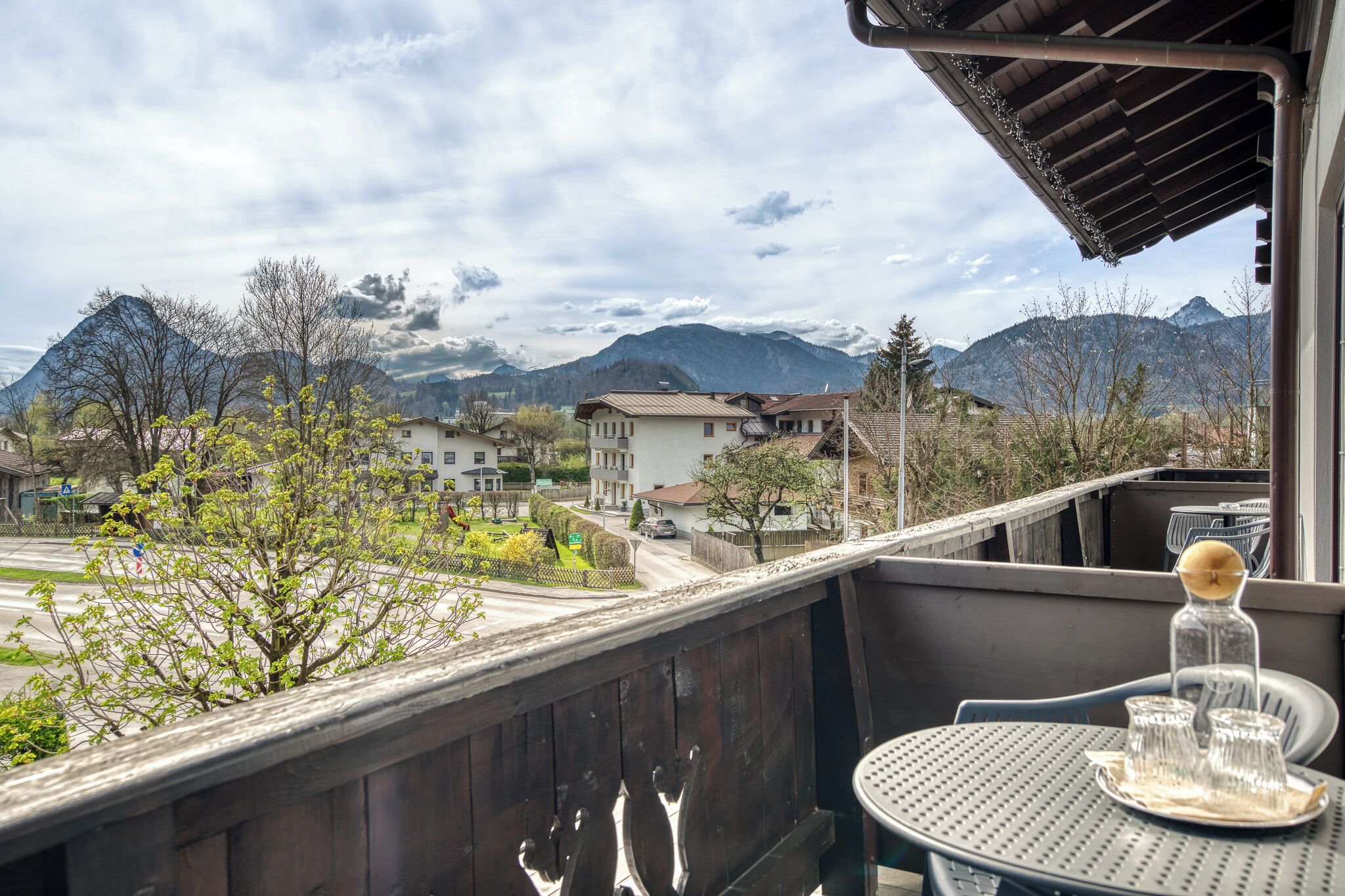 A balcony with a table and chairs, overlooking a street and mountains.