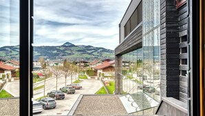 Vista desde una ventana con perspectiva a una calle residencial con casas y coches aparcados, con montañas al fondo.