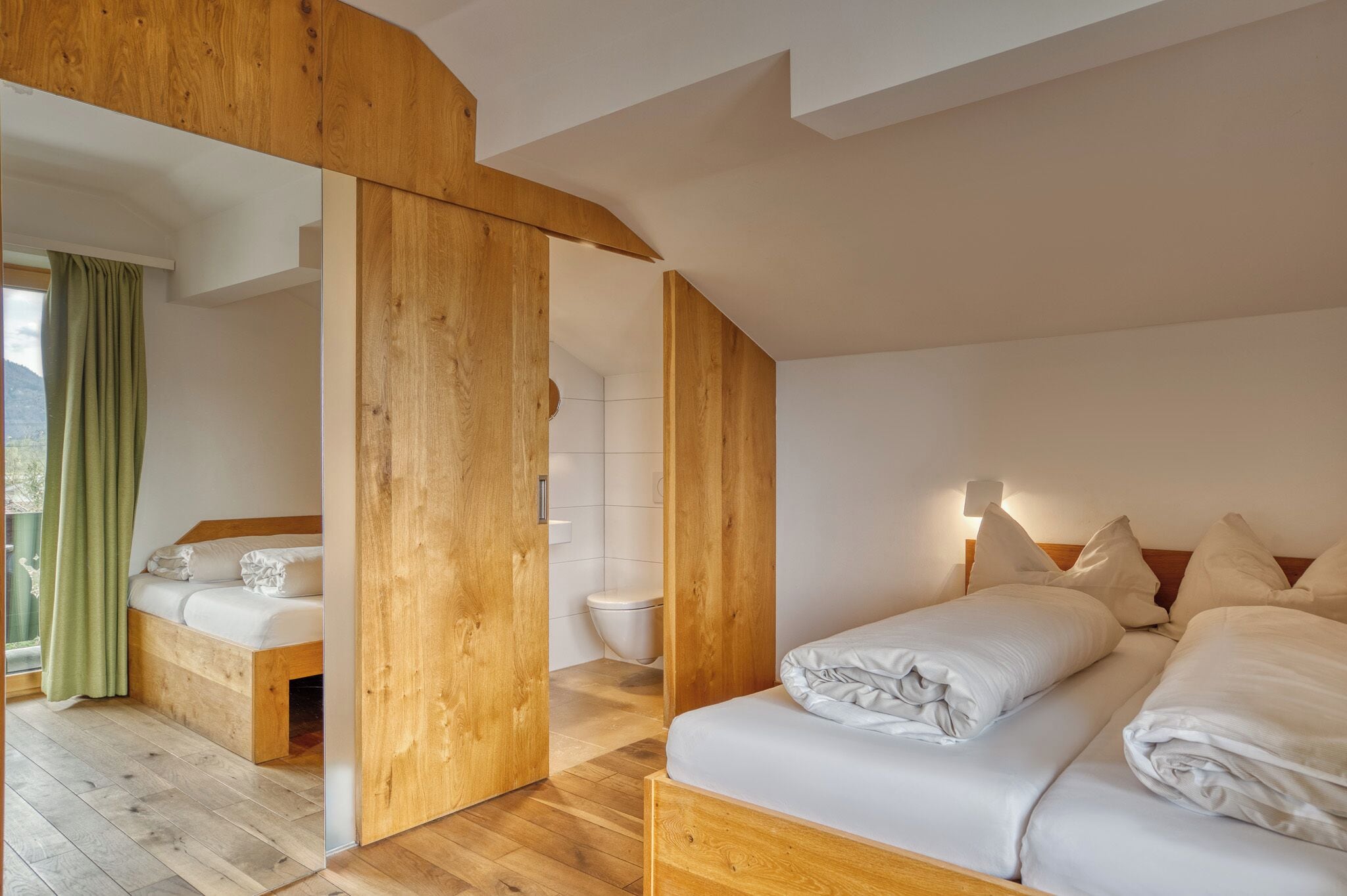 A modern bedroom with a wooden ceiling, a large bed, a smaller bed, and a bathroom.