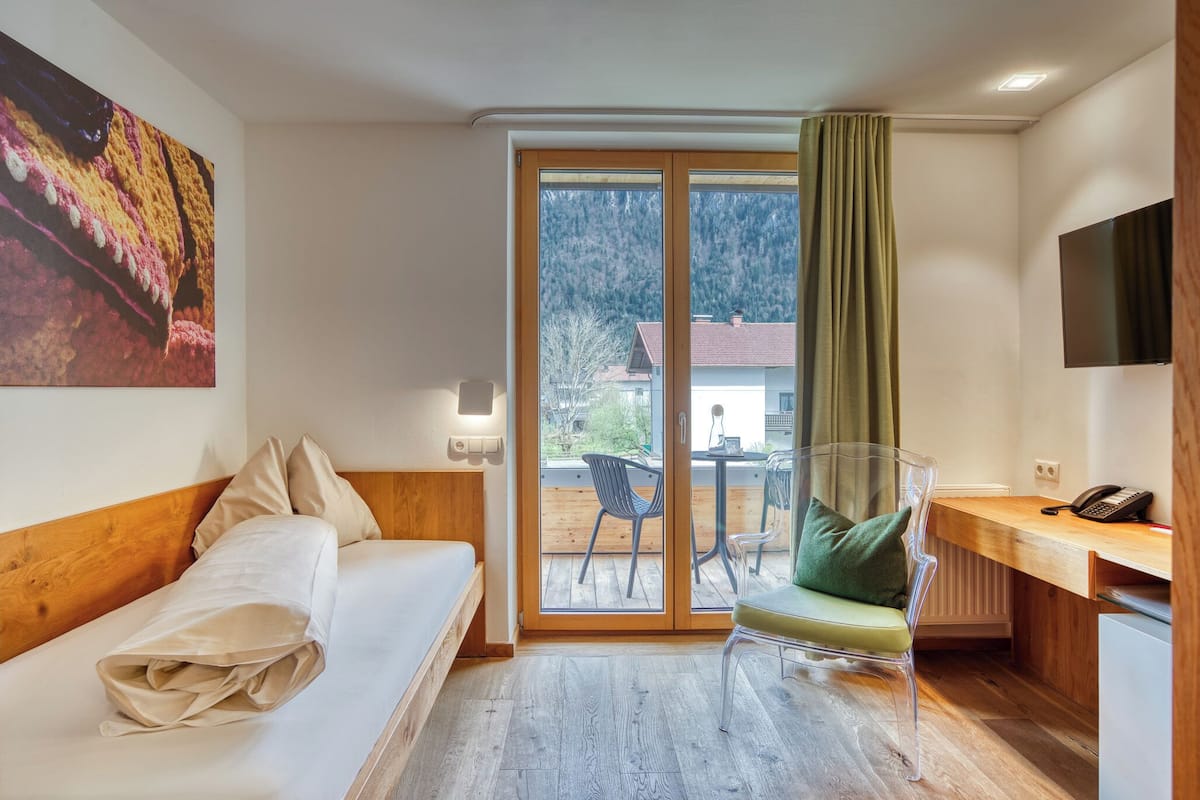 A hotel room with a bed, a desk, a chair, a TV, and a view of the outdoors.