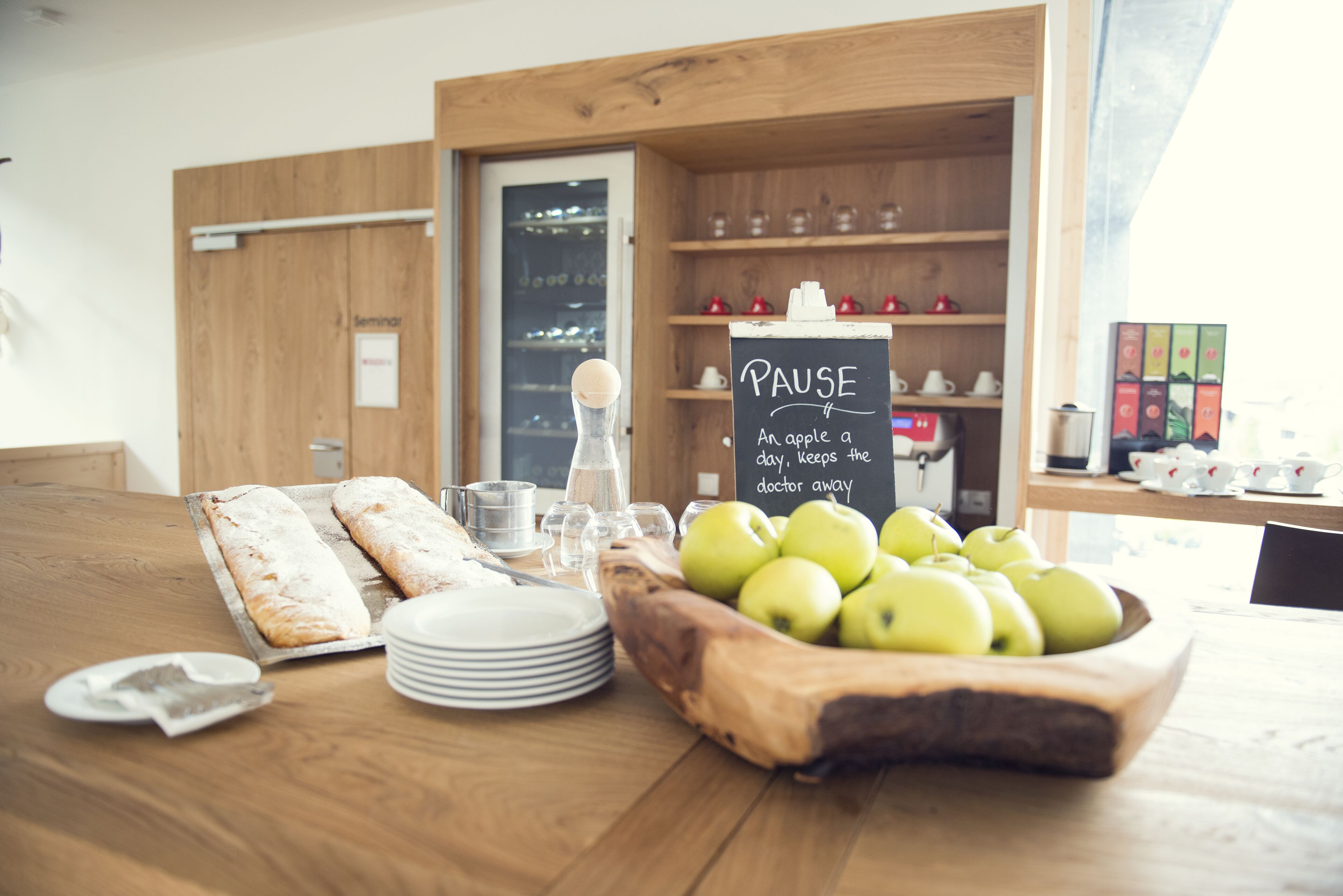 Una disposición para el desayuno con pan, manzanas y un cartel que dice “PAUSE Una manzana al día mantiene al médico a distancia.”