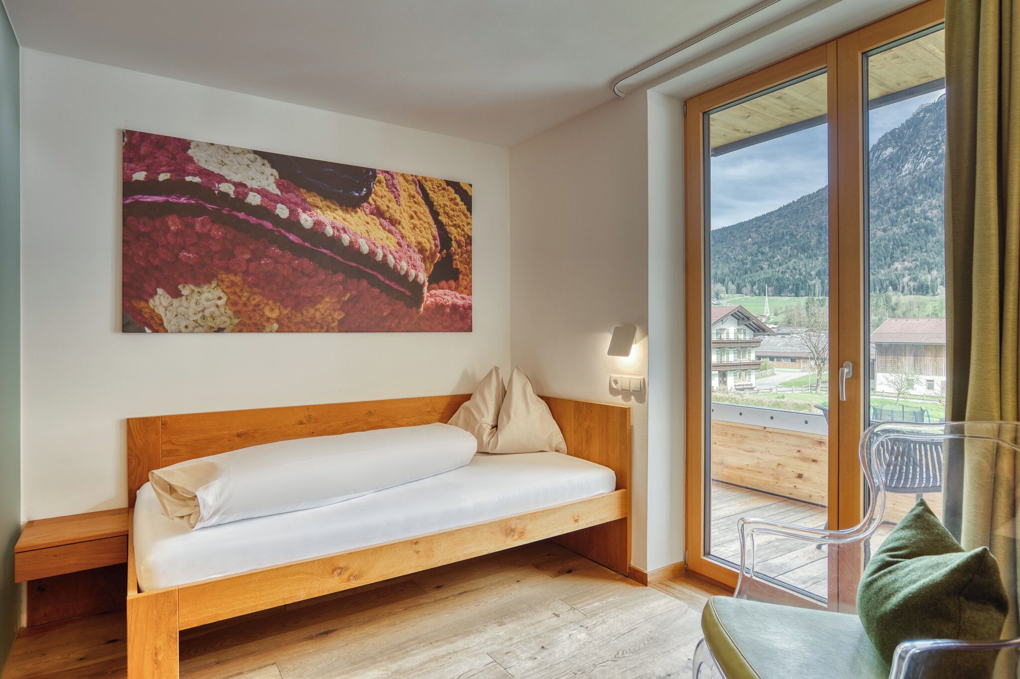 Una habitación con una cama de madera, un ventanal con vistas a una montaña y edificios, y un cuadro en la pared.