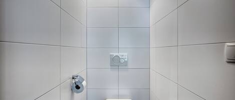 Un baño moderno con azulejos blancos, un inodoro, un dispensador de papel higiénico en la pared y un perchero para toallas.