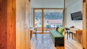 Una habitación moderna con piso de madera, un sofá verde, un escritorio y un televisor montado en la pared.