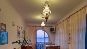 Quarto com chão xadrez, móveis de madeira, sofá verde riscado, mesa de madeira e vista para o mar através de uma grande janela.