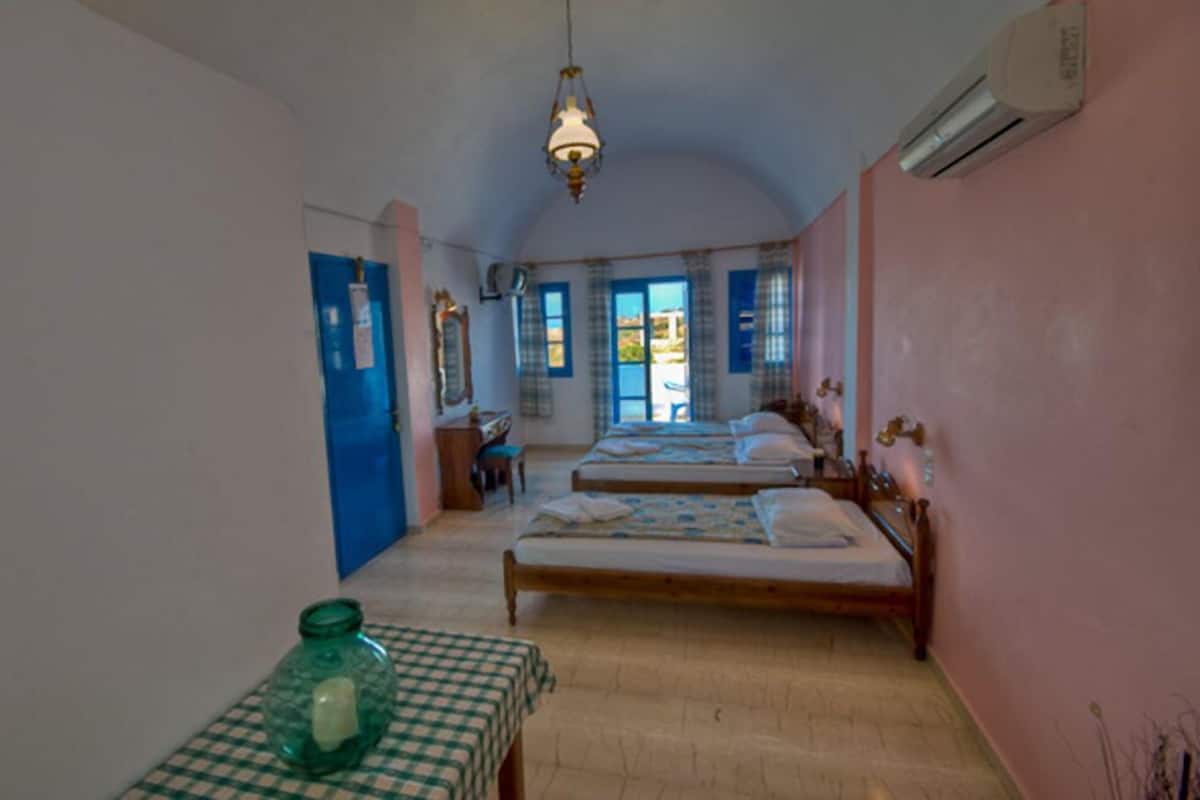 A room with two beds, a table with a checkered tablecloth, a green vase, and a hanging light fixture.