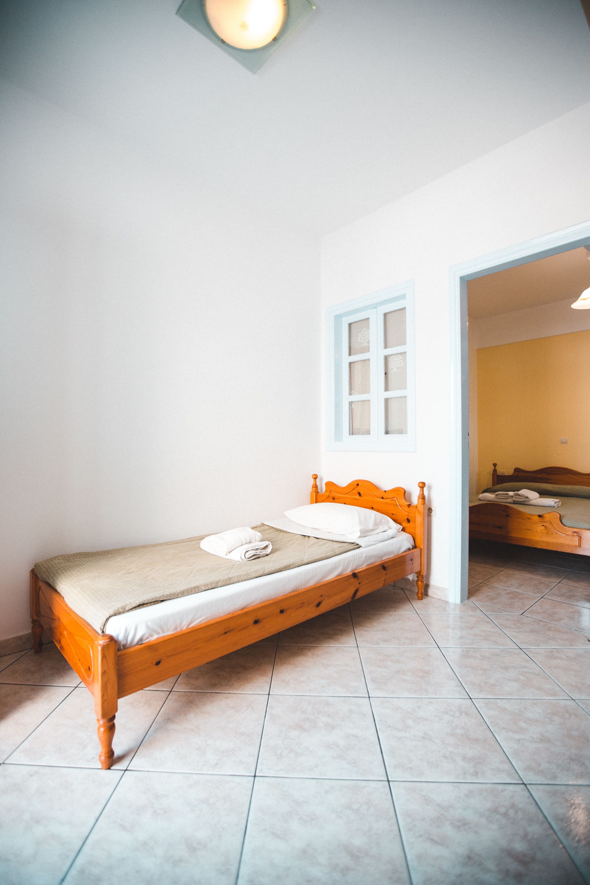 A single bed with a wooden headboard in a room with white walls and a tiled floor.