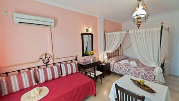 Un dormitorio con cama, escritorio, silla, mesa con bandeja, aire acondicionado, espejo y candelabro.