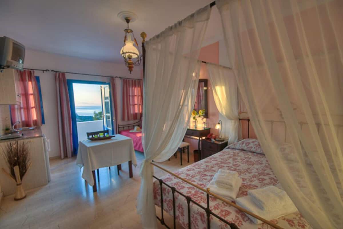 A bedroom with a bed, a desk, a chair, a table, and a view of the sea.