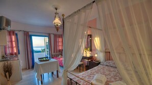 Quarto com cama, escrivaninha, cadeira, mesa e vista para o mar.