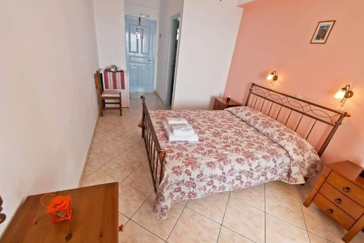 A bedroom with a bed, a chair, a wooden nightstand, and a door leading to another room.