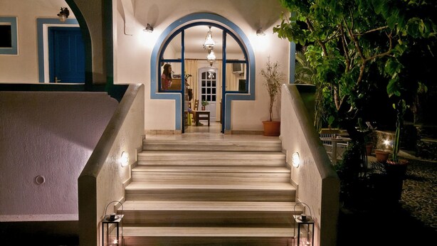Uma escadaria leva a um quarto com uma porta azul, um vaso de planta e um candelabro.