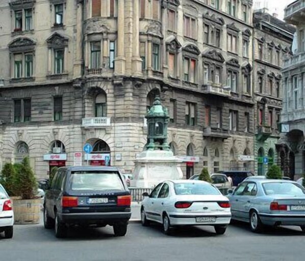 A street view with cars parked in front of a historic building with ornate architecture and a statue in the center.