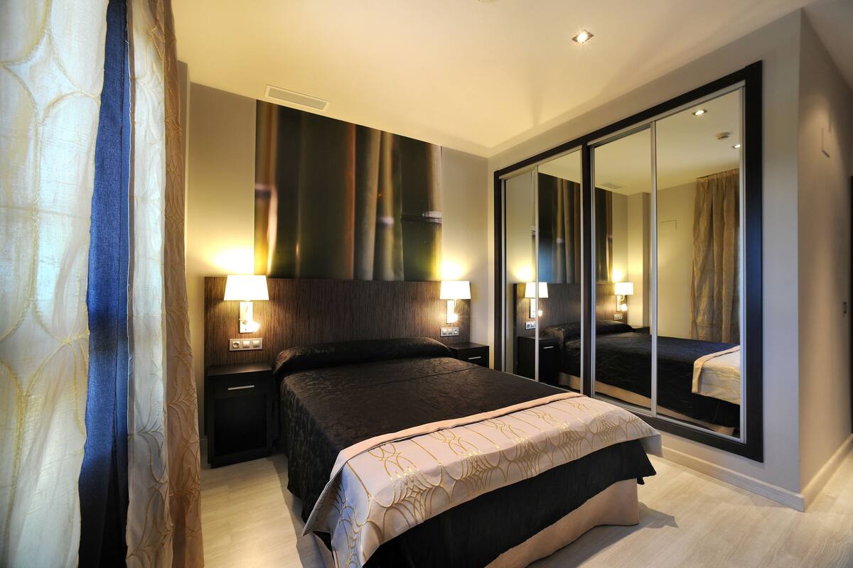 A modern bedroom with a large bed, two bedside lamps, a mirror, and a sliding door closet.