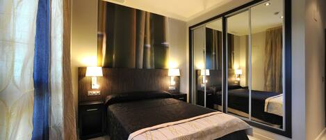 A modern bedroom with a large bed, two bedside lamps, a mirror, and a sliding door closet.
