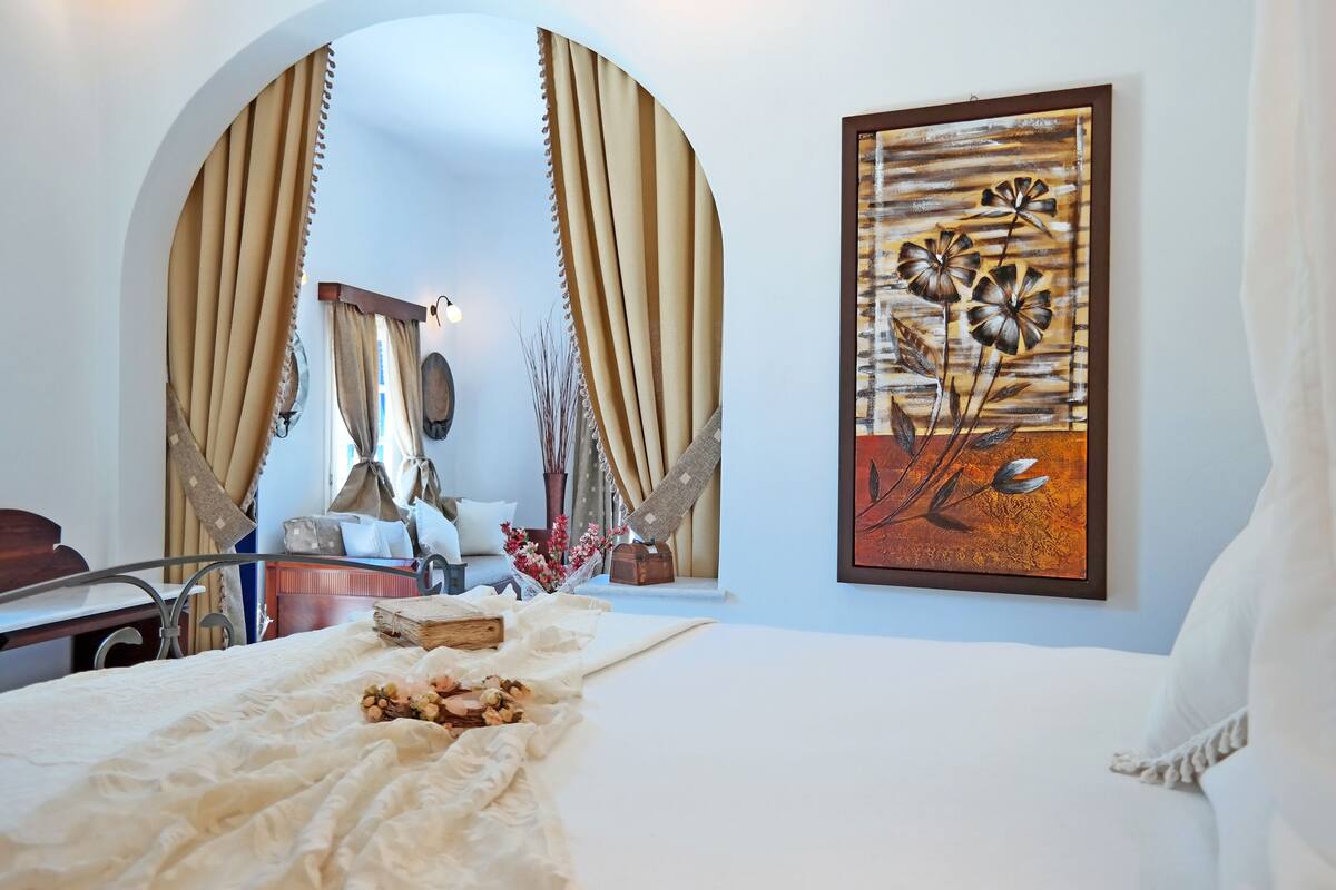 A bedroom with a bed, curtains, a painting, and a bedside table.