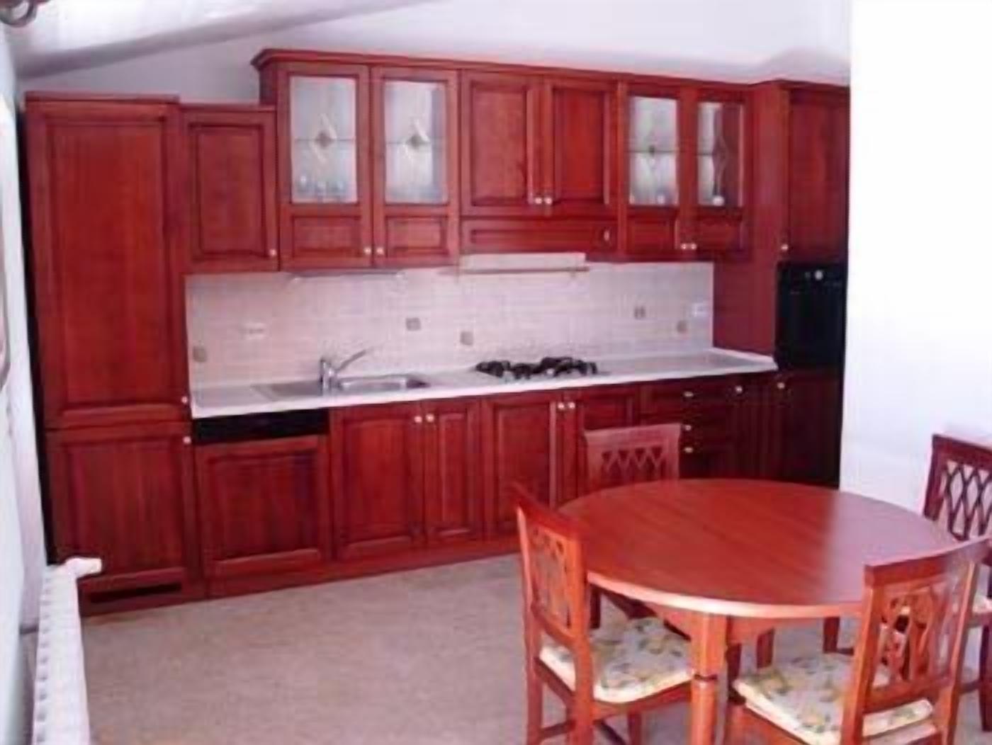 A compact kitchen with wooden cabinets, a white countertop, and a dining table with chairs.