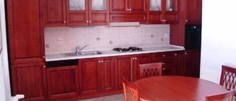 A compact kitchen with wooden cabinets, a white countertop, and a dining table with chairs.