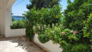 A balcony with a view of the sea, surrounded by lush greenery and flowering plants. - Apartments and rooms Rogosic (Hvar)