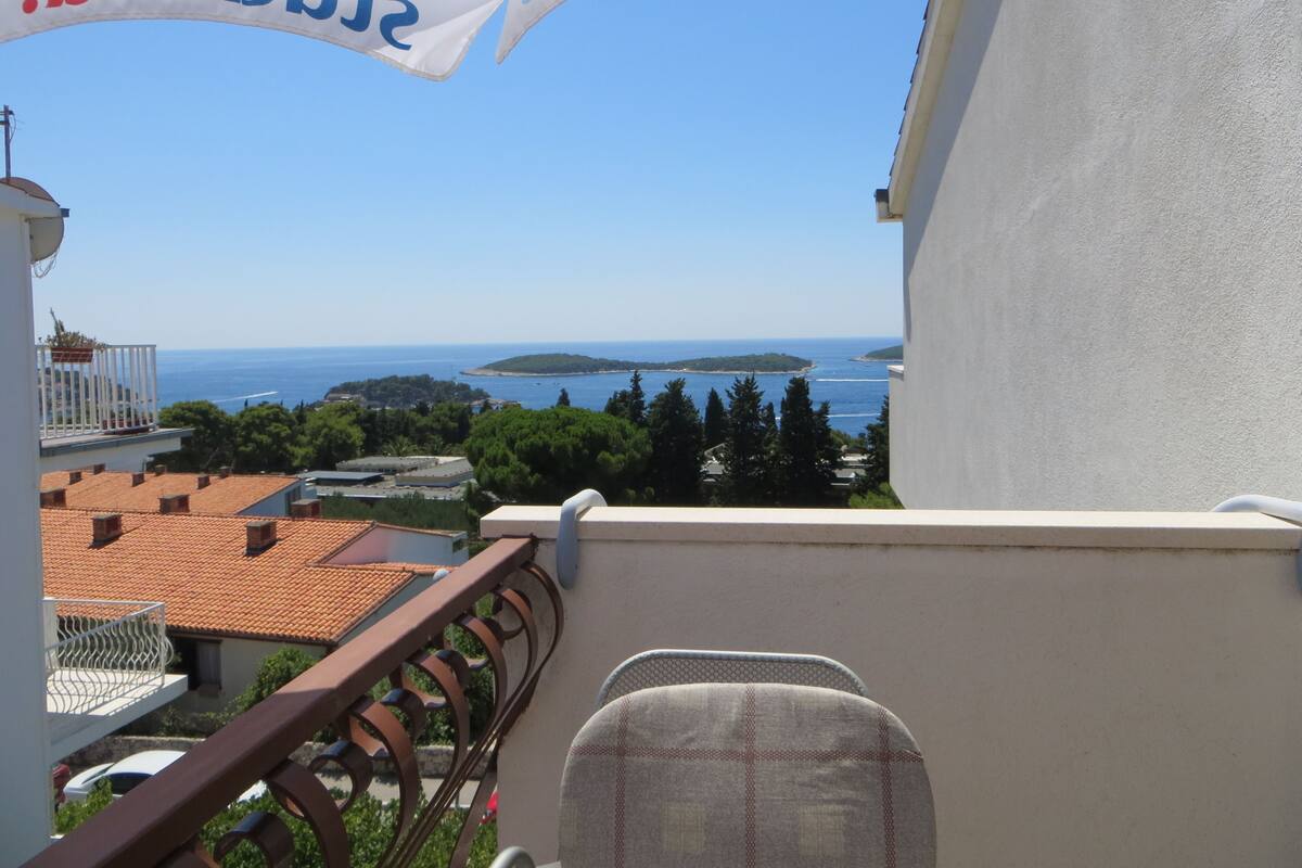 A balcony with a view of the sea and islands, a white umbrella, and a chair.