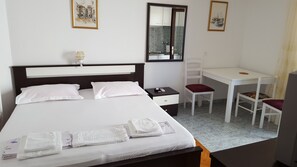 A neatly made bed with pillows, a bedside table with a remote control, a desk with a chair, and a mirror on the wall.