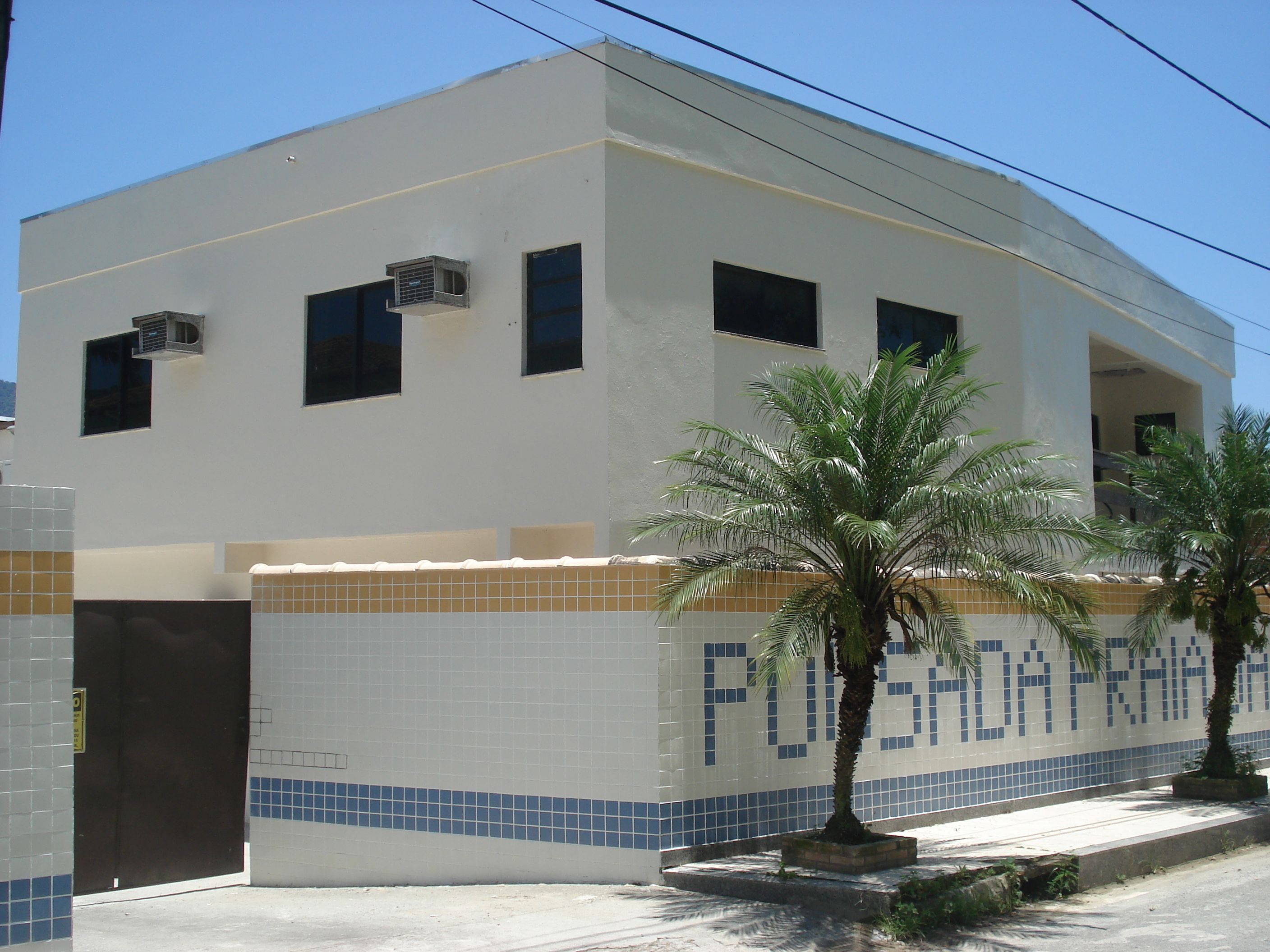 A building with a tiled facade, air conditioning units, and a palm tree in front.