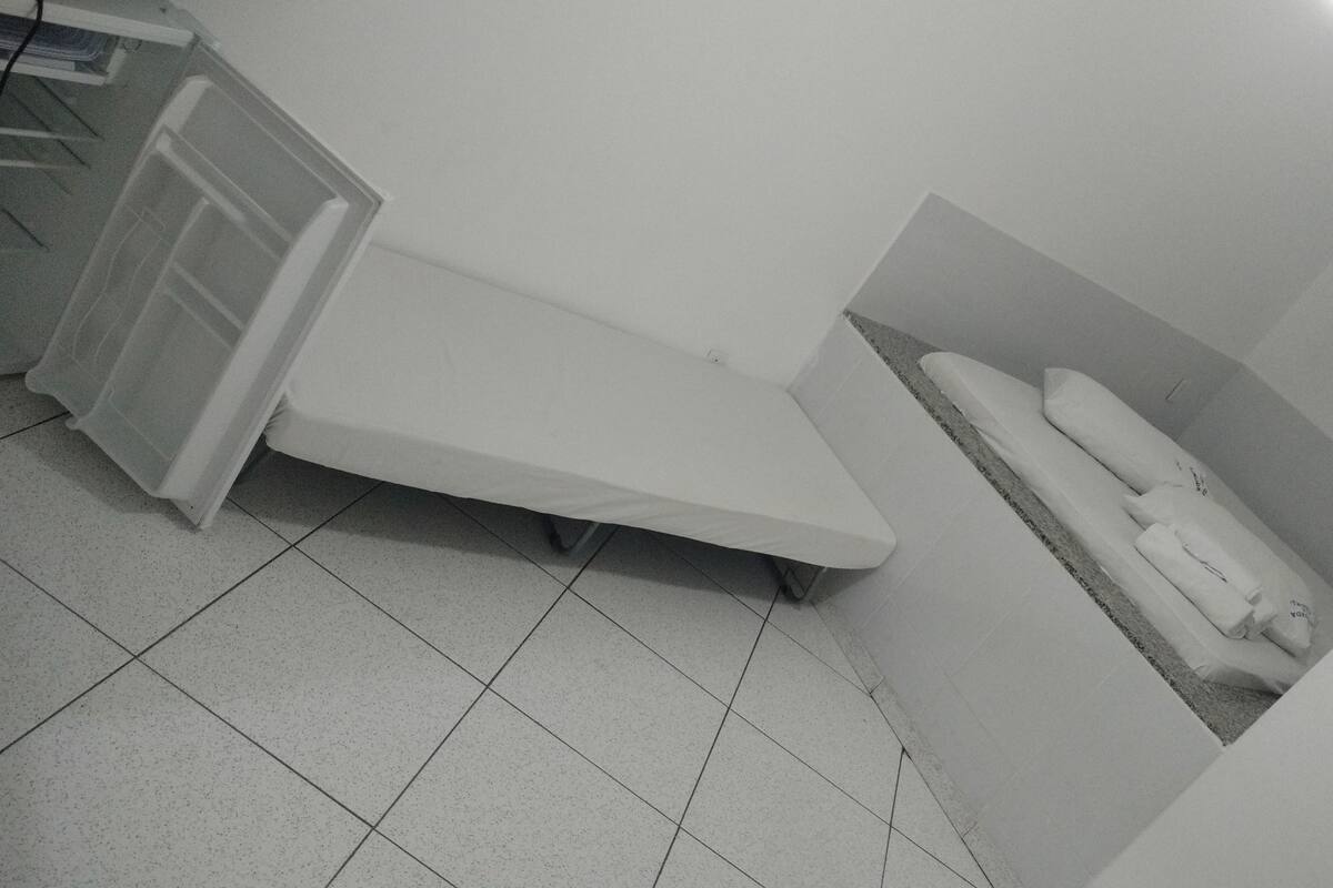 A small, dimly lit room with a bed, a small table, and a cabinet.