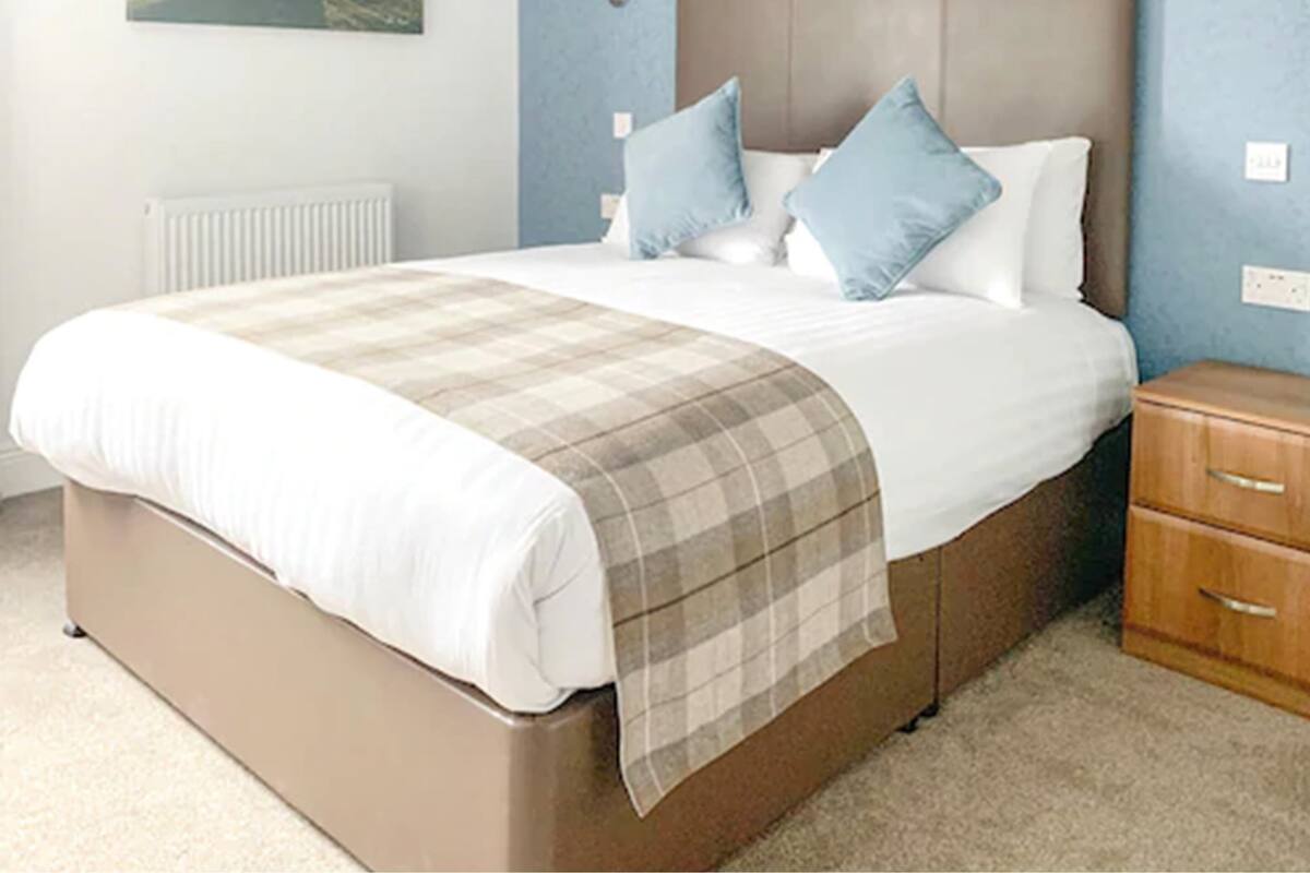 A bedroom with a large bed, a headboard, bedside lamps, a nightstand, and a painting on the wall.