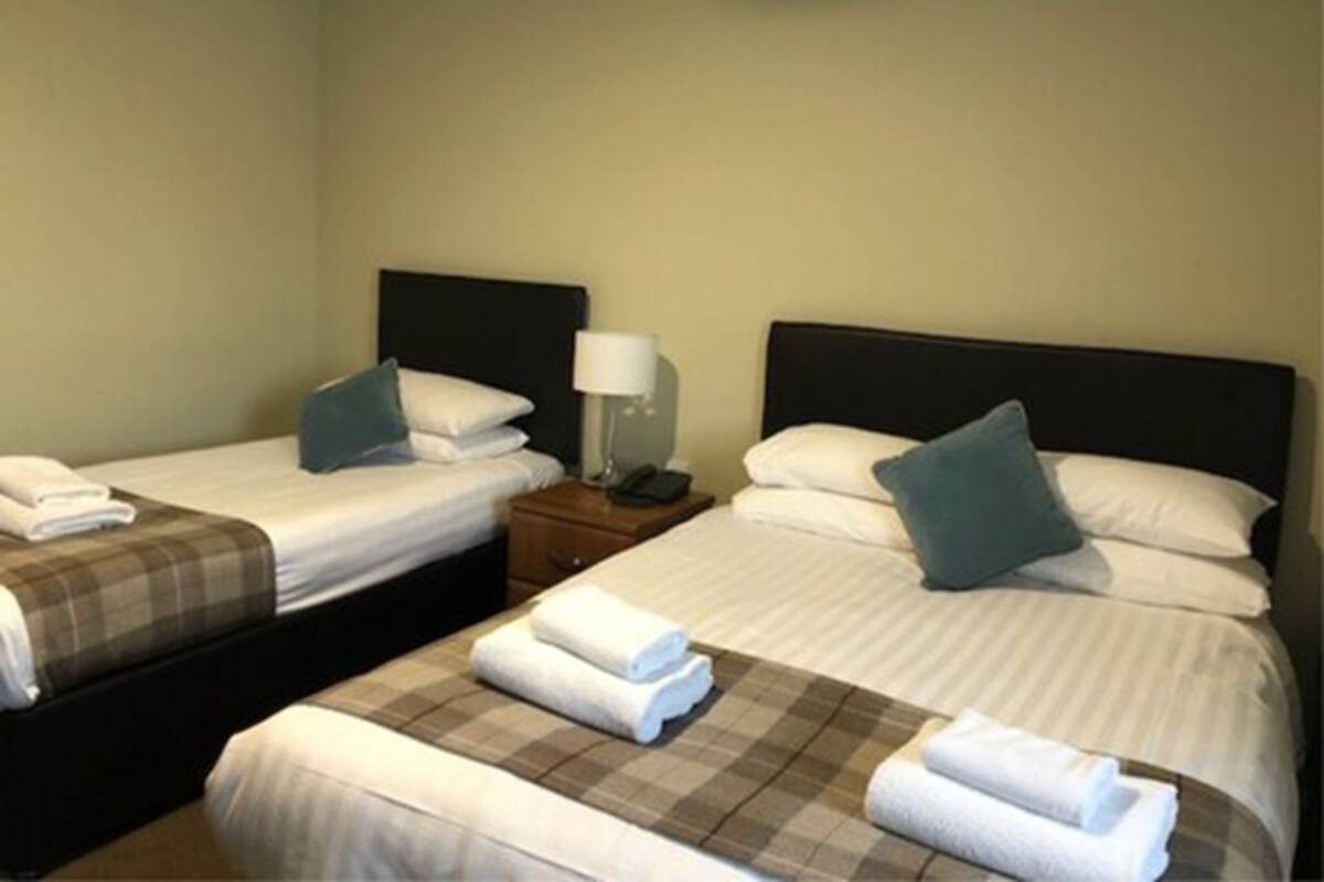 A hotel room with two single beds, each with a pillow and a bedside table with a lamp.