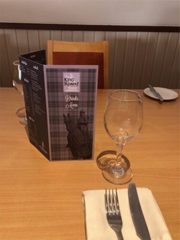 Una mesa con un menú, una copa de vino y cubiertos.