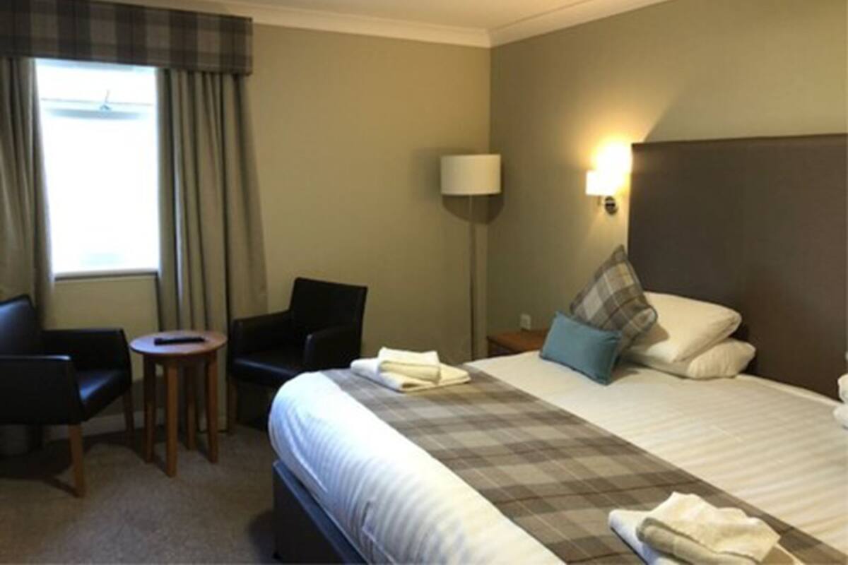 A hotel room with a bed, a chair, a small table, a lamp, and a window with curtains.