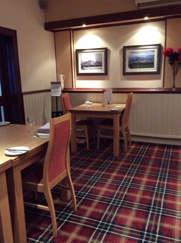 A dining area with a plaid carpet, wooden furniture, and framed pictures on the wall. - King Robert Hotel (Stirling)