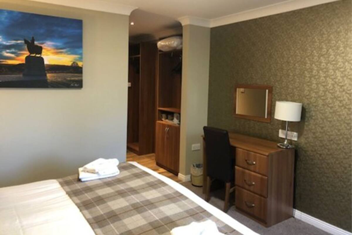 A hotel room with a bed, a desk, a chair, a wardrobe, and a painting of a sunset.