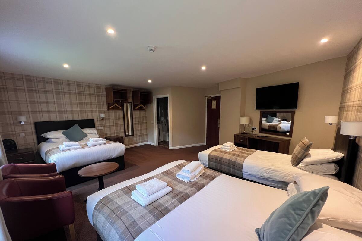A hotel room with two beds, a desk, a chair, and a TV.