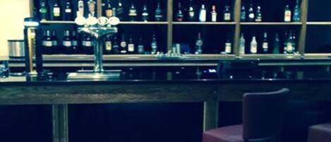 A bar area with a wooden counter, shelves of liquor bottles, and two bar stools.