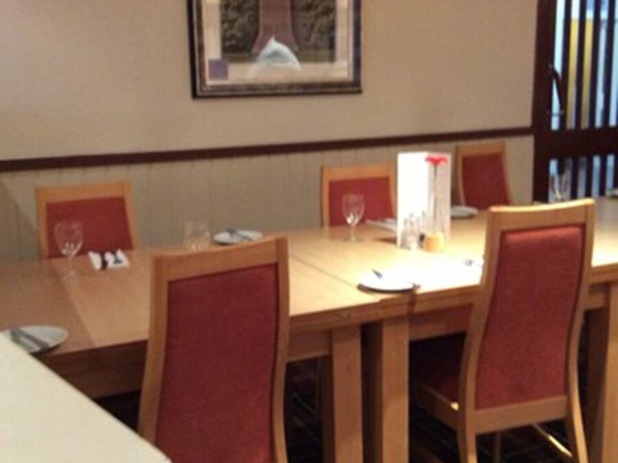 A dining area with a wooden table and red upholstered chairs, a framed picture on the wall, and a plaid carpet.