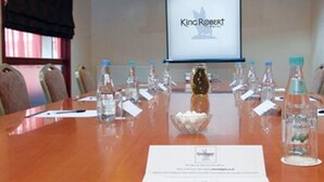 Un salón de conferencias con una mesa de madera, botellas de agua y una pantalla de proyector mostrando 'KingRobert'.